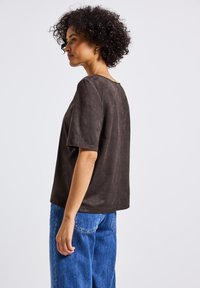 Top corto in suede marrone con scollatura rotonda, vestibilità comoda e texture liscia, abbinato a jeans blu di denim larghi.