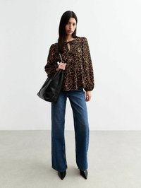 Blouse à imprimé léopard marron avec un décolleté en trou de serrure, associée à un jean en denim à jambes larges et un sac fourre-tout en cuir noir. Chaussures noires pointues.