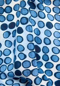 Blauer Stoff mit einem durchgehenden Muster aus unterschiedlich großen, kreisförmigen Formen in dunkleren und helleren Blautönen auf hellblauem Hintergrund.