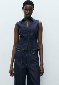 Denimvest met mouwloos ontwerp, donkerblauwe kleur, gedetailleerde stiksels, peplum zoom, gecombineerd met bijpassende loszittende denim broek.