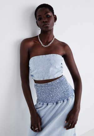 Conjunto de dos piezas de denim azul claro que incluye un top corto sin tirantes y una falda con fruncidos. Textura suave con ligeras variaciones en el color.