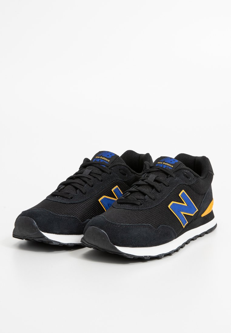 Zapatillas deportivas negras con materiales de malla y ante, que cuentan con acentos en azul y amarillo, una suela texturizada y un prominente logo "N" en el lateral.