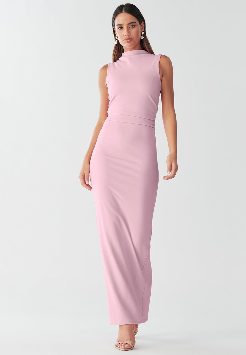 Kaftaan vaale pink rang ka maxi dress jiski ooncha galla hai, bina baaho ke design, mulayam textures aur zameen tak lambai. Yeh ik bhaari kamar band ke saath sajaya gaya hai.