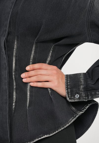 Temna denim srajca z oprijetim krojem, svetlim šivom, ukrivljenim robom in zaprtimi manšetami. Tkanina ima mehak, teksturiran zaključek.