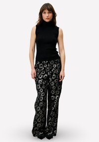 Zwart geribd mouwloos topje met een hoge hals, gecombineerd met wijduitlopende broek met bloemenpatroon in zwart en metallic zilver. Gladde textuur.