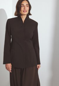 Čierny sakový kabát s vypnutým golierom, dlhými rukávmi a dvoma prednými vreckami. Vyrobené z hladkej tkaniny so štruktúrovaným dizajnom.