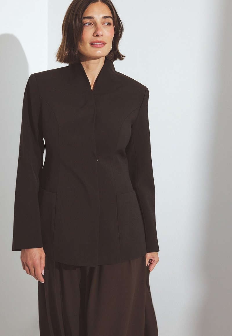 Čierny sakový kabát s vypnutým golierom, dlhými rukávmi a dvoma prednými vreckami. Vyrobené z hladkej tkaniny so štruktúrovaným dizajnom.