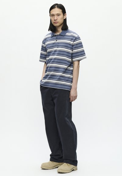 Chemise polo rayée bleu et blanc, pantalon noir ample et chaussure beige. Style décontracté avec des manches courtes et un col.