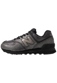 Schwarzer Sneaker mit einer strukturierten metallisch-silbernen Oberfläche, schwarzen Schnürsenkeln und einer Gummisohle mit Rillen; auffälliges "N"-Logo an der Seite.