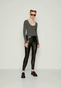 Γκρι κορμάκι με μακρύ μανίκι, μαύροι ψηλόμεσοι παντελόνια από ψεύτικο δέρμα και χοντρά μαύρα παπούτσια. Συνδυασμένο με ορθογώνια κόκκινα γυαλιά ηλίου.