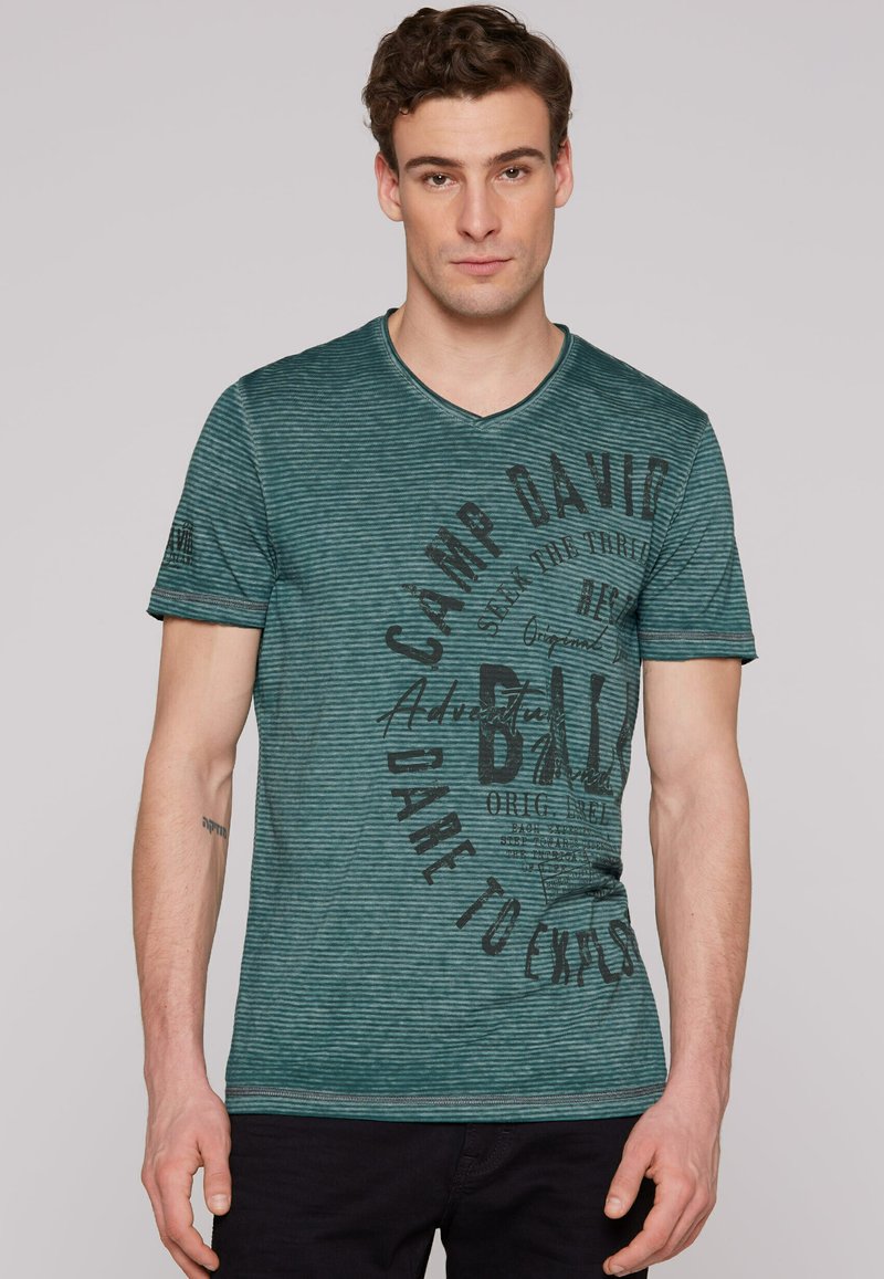Camiseta de rayas verde azulado con escote en V, que presenta texto y gráficos impresos en negro en el frente, mangas cortas y un corte relajado.