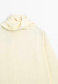 Langsleeve, lichtgele top met een gedrapeerde halslijn, zachte textuur en een ontspannen pasvorm met een gladde stofafwerking.