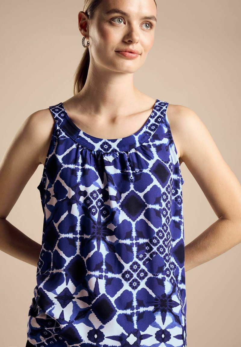 Marinblå ärmlös topp i lätt material med ett geometriskt mönster och vita accenter samt en rynkad halsringning.