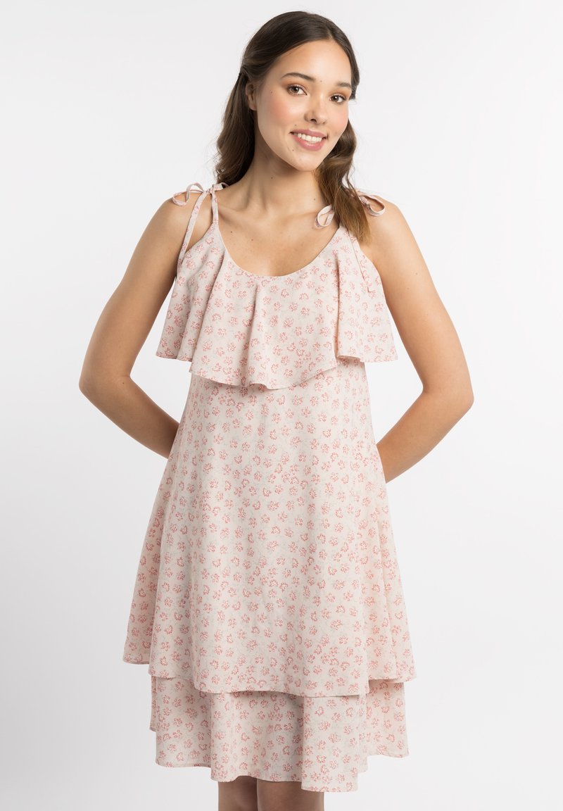Bloemenprint jurk in lichtroze met gelaagde ruches. Voorzien van verstelbare strikbanden en een knie-lange zoomlijn voor een vloeiende silhouette.
