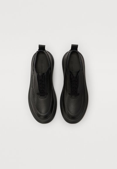 Sneakers negre din piele cu o suprafață texturată, șireturi plate, manșetă și tălpi căptușite. Design minimalist și formă rotunjită.