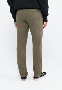 Chinos vert olive avec une coupe droite, deux poches arrière et une fermeture éclair. Paire de baskets noires avec des accents blancs visibles en bas.