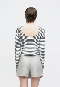 Czarna i biała bluzka w paski z długim rękawem i niskim, wyciętym tyłem, zestawiona z jasnoszarymi, wysokim stanem szortami. Prosty, dopasowany krój.