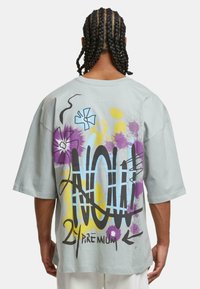 Světle šedé oversized tričko s barevným graffiti designem, na kterém jsou květiny, abstraktní tvary a text na zadní straně.