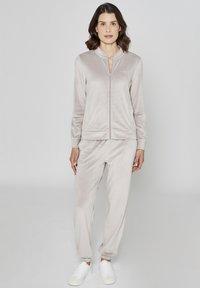 Jasnoszary welurowy dres z kurtką na suwak i spodniami z elastyczną talią. Gładka faktura, dopasowany krój i ściągacze na rękawach. Białe trampki.