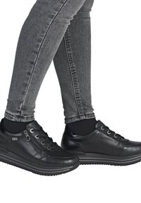 Black leather sneakers with a smooth texture, round toe, lace-up design, and side zippers, paired with form-fitting grey jeans.