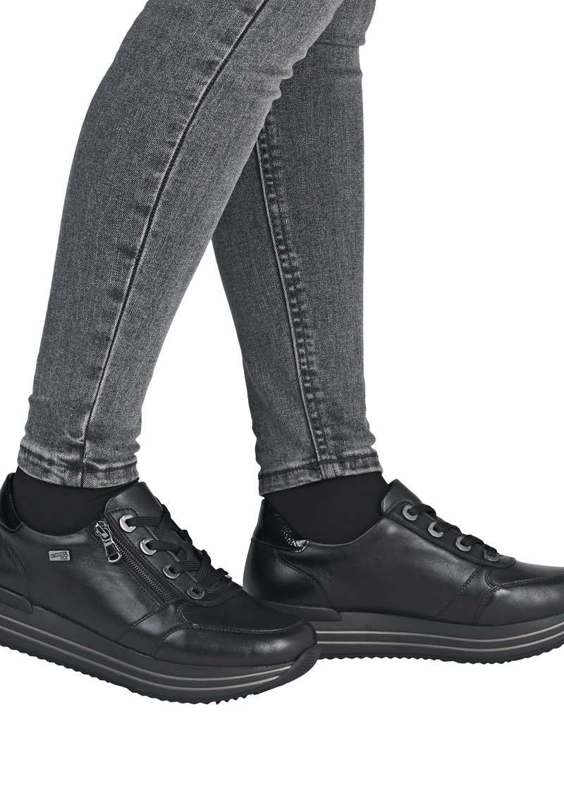 Black leather sneakers with a smooth texture, round toe, lace-up design, and side zippers, paired with form-fitting grey jeans.