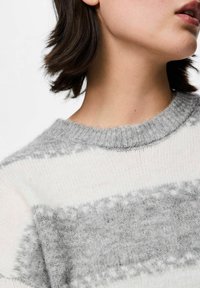Grå och vit randig stickad tröja med rund halsringning, som har en mjuk textur och subtila mönsterdetaljer. Närbild.