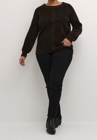 Braun-schwarz gestreifter Strickpullover mit rundem Ausschnitt, kombiniert mit schwarzen Skinny-Jeans und Stiefeletten vor neutralem Hintergrund.
