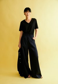 Zwarte V-hals T-shirt gecombineerd met loszittende marineblauwe wijde broek. De broek heeft een elastische tailleband en zijzakken, casual gedragen met sandalen.