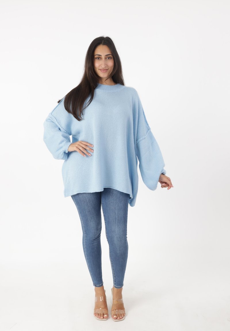 Hellblauer, übergroßer Pullover aus weichem Material mit weiten Ärmeln und rundem Ausschnitt, kombiniert mit enganliegenden blauen Jeans und klaren Sandalen.
