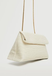 Biała torebka o fakturowanej powierzchni w kształcie trójkąta z klapą. Posiada złotą łańcuszkową rączkę i subtelne wytłoczone detale na powierzchni.