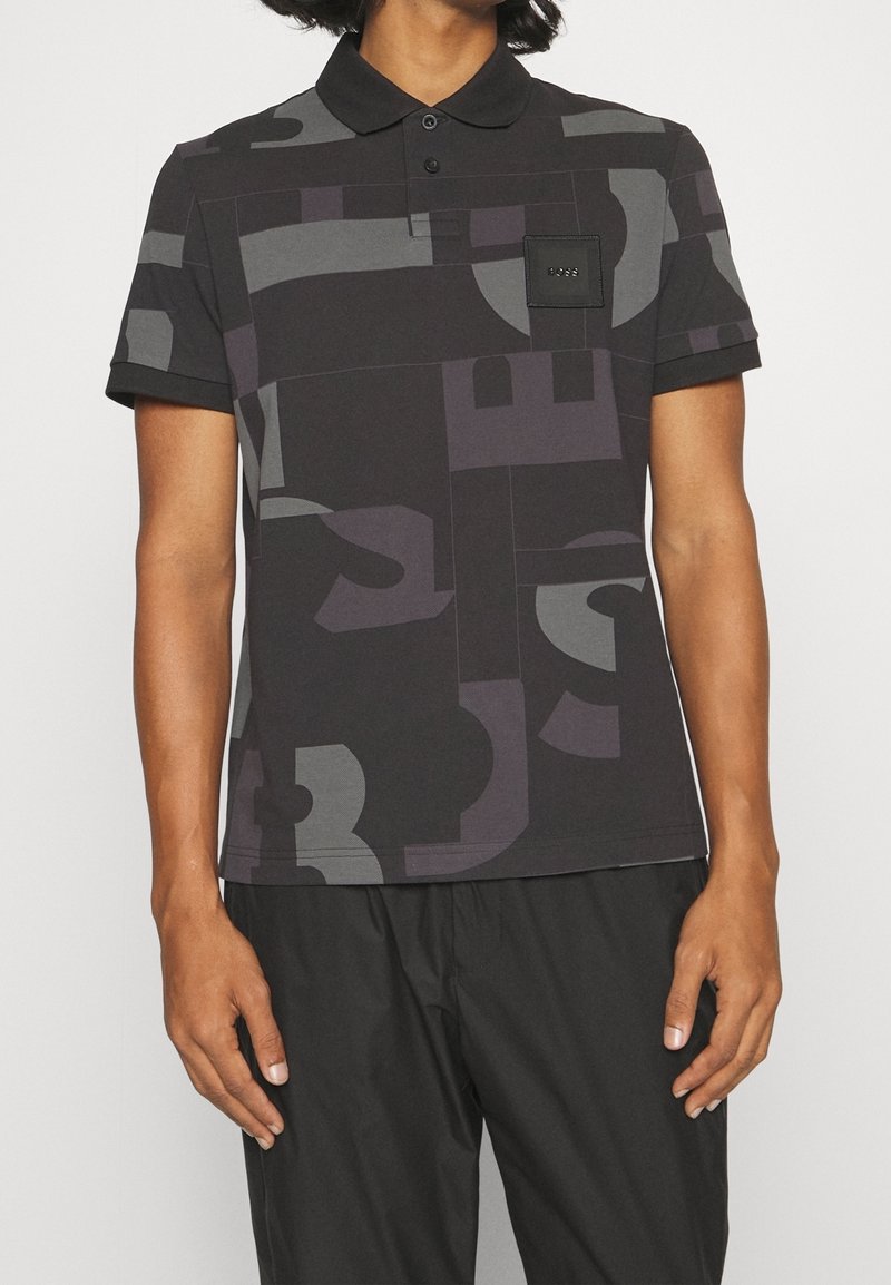 Polo à manches courtes noir avec motifs abstraits en blocs gris, patte de boutonnage et une poche poitrine ornée d'un logo carré noir.