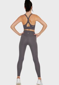 Set atletico grigio composto da un reggiseno sportivo con design a schiena scoperta e ritaglio, abbinato a leggings a vita alta. Tessuto morbido e liscio.