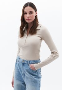 Beige geribbelde lange mouwen top met een ritskraag, gedragen met lichtblauwe high-waisted jeans, voorzien van een voorzak en een relaxed fit.