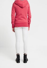 Roze hoodie met fleece voering en een trekkoord, gedragen over witte skinny jeans, gecombineerd met zwarte enkellaarsjes met zijknippers.