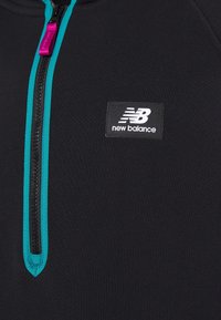 Pullover nero con cerniera a tutto davanti, dettagli turchesi e zip rosa. Presenta una toppa rettangolare con il logo New Balance sul petto. Texture liscia.