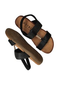 Zwarte platte sandalen met textuur-elastische enkelriemen, decoratieve gouden spiraaldetails en gebosseleerde bruine rubberen zolen, weergegeven van boven en onder.