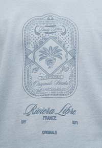 Σχεδιασμός κειμένου σε ύφασμα με διακοσμητικό έμβλημα αγγείου, "Jack & Jones Originals Studio," "Riviera Libre France," και τις λέξεις "Off Duty Originals."