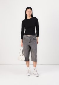 Schwarzes, langärmliges, tailliertes Oberteil, graue, kurze Jeanshose, weiße High-Top-Sneaker, kleine weiße Handtasche. Einfaches Design, weicher Stoff.