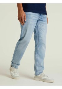 Vaqueros de mezclilla azul claro con un corte relajado, presentando un corte recto y sutiles detalles de desgaste. Combinados con zapatillas blancas.