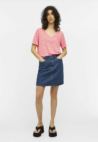 T-shirt à manches courtes en V rayé rouge et blanc, associé à une jupe en denim bleu foncé, accentuée par deux poches avant. Sandales à plateforme noires.