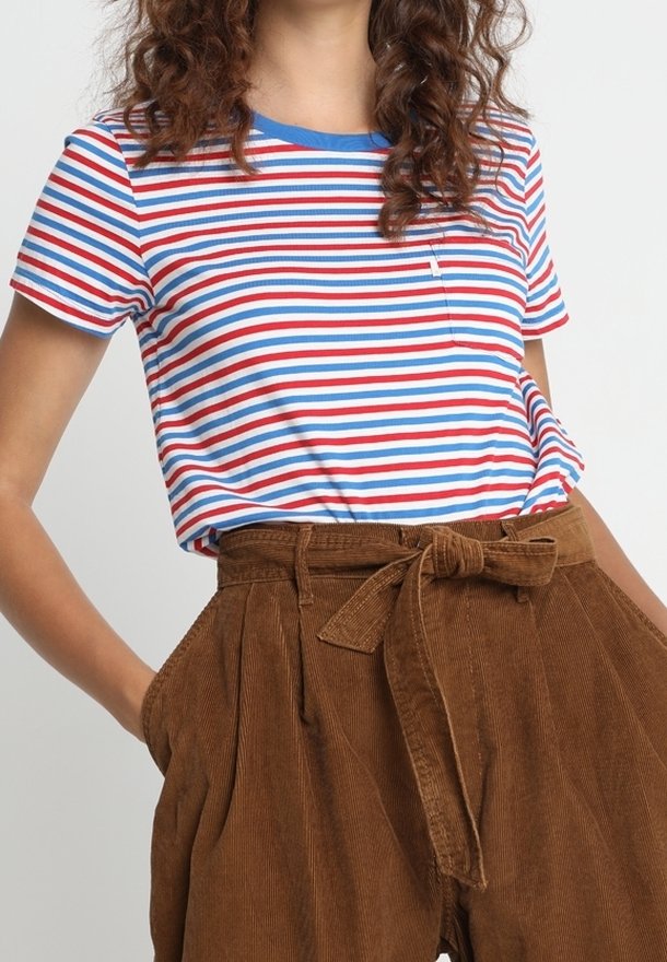 Femme portant un t-shirt rayé rouge, blanc et bleu, rentré dans un pantalon en velours côtelé marron taille haute avec une ceinture nouée.