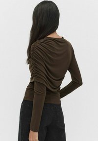 Ruskea pitkähihaisessa paidassa on kerrottu tekstuuri selkäpuolella, tiukka malli ja pehmeä kangas. Yhdistetty tummiin farkkuihin, joissa on tikkaus yksityiskohtia.