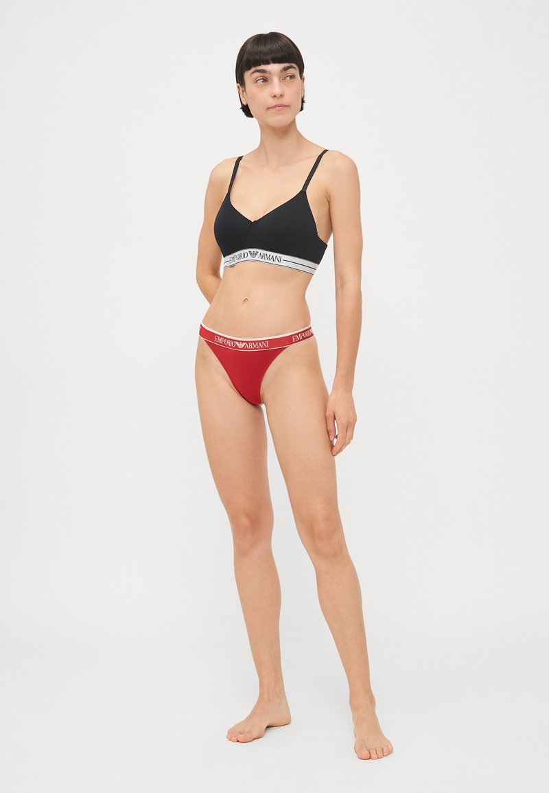 Black bralette with gray and white band; red thong with white logo band. Smooth fabric, minimalist design, featuring adjustable straps.