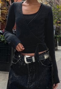 Černý zavinovací svetr s texturovaným povrchem přes žebrované tílko, kombinovaný s vysokým pasem černých džín a černým opaskem s hroty a stříbrnou přezkou.