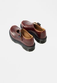 Hnedé kožené topánky s textúrovaným povrchom, vybavené kruhovým výrezom a detailom s prackou, umiestnené na čiernej gumenej podrážke.