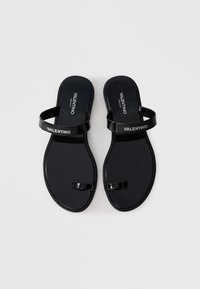 Black flat sandals with a glossy finish, featuring two wide straps and a toe post. "Valentino" logo displayed on the strap.