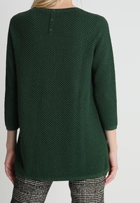 Maglione verde strutturato con maniche a tre quarti, caratterizzato da un collo arrotondato e un dettaglio con tre bottoni sul retro.