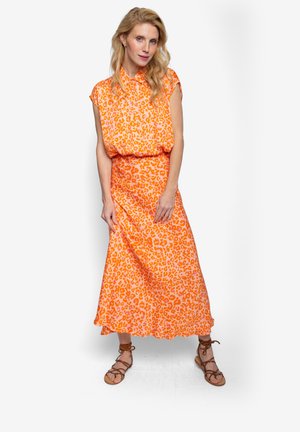 Pomarańczowa sukienka z nadrukiem w panterkę, z kołnierzykiem i rozkloszowanym dołem. Wykonana z lekkiego materiału; zestawiona z brązowymi sandałami.