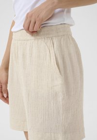 Shorts beiges en tissu texturé et froissé, dotés de poches latérales et d'une taille élastique pour plus de confort. Design simple et décontracté.