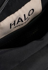 Svart tyginteriör med en synlig krämfärgad etikett märkt "HALO" och siffrorna "196819721981" i fet svart text. Texturerad foder finns.